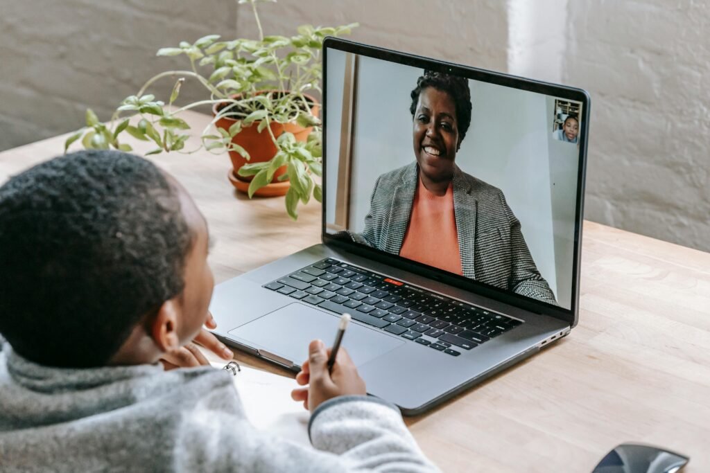 A child participates in online tutoring, focusing on a laptop screen with a smiling tutor.